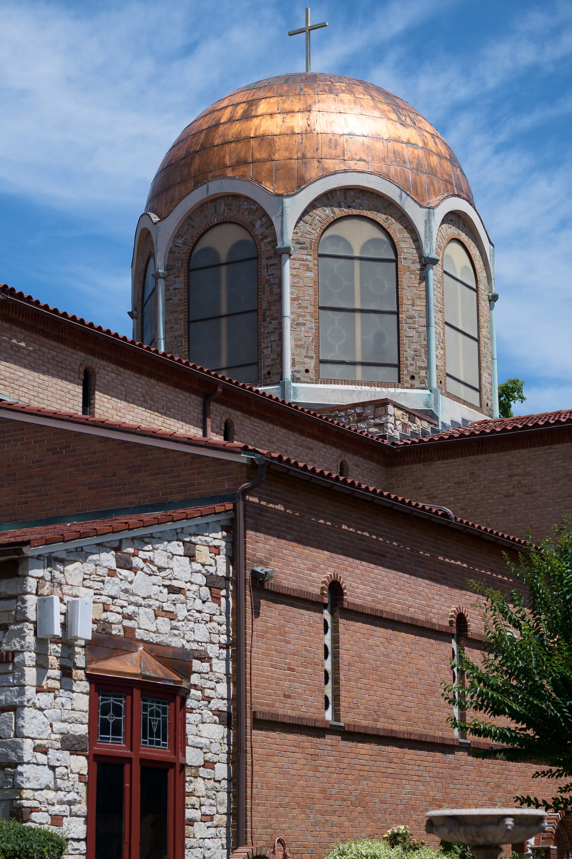 The church's copper dome and bell cross against a blue sky, above the brick and stone facade.